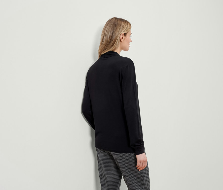 Une femme vue de dos porte un t-shirt noir à manches longues et un pantalon à motif pied-de-poule.