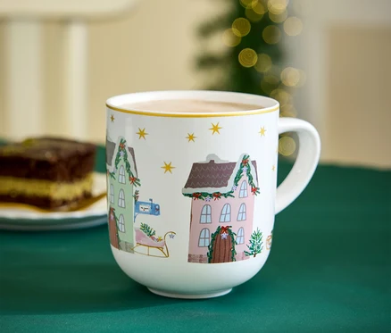 Une tasse avec des motifs de Noël est posée sur une nappe verte à côté d'une part de gâteau.