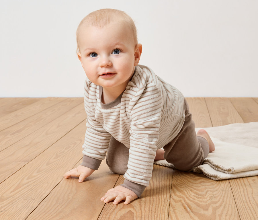 Un bébé rampe sur un plancher en bois dans un ensemble en nicki.