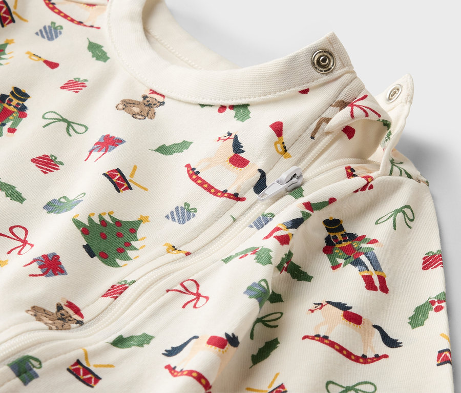 Gros plan sur un pyjama de bébé avec des motifs de Noël, une fermeture éclair et des boutons-pression.