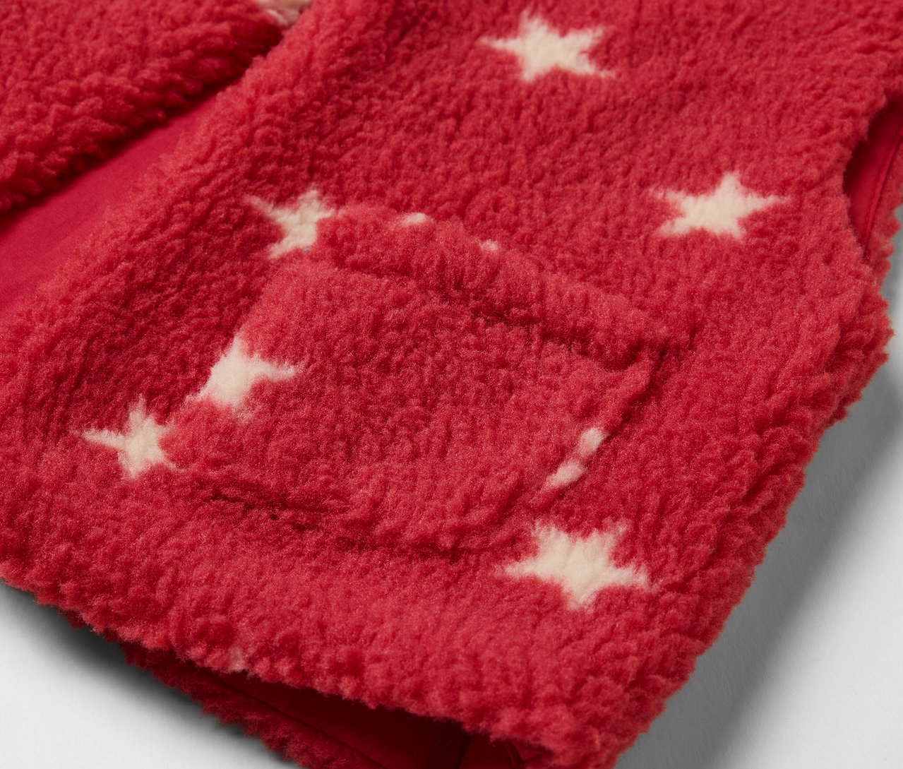 Détail d'un gilet sans manches enfant en polaire teddy rouge avec des étoiles blanches et une poche.
