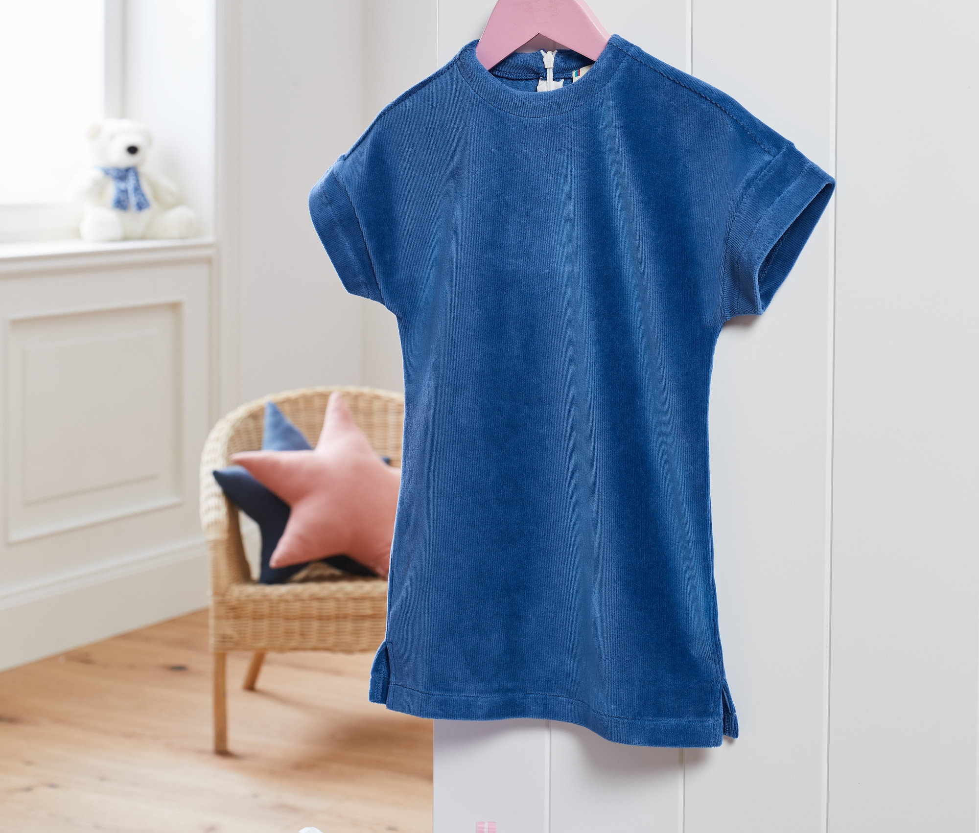 Une robe stretch en velours côtelé bleue est suspendue à un cintre rose.