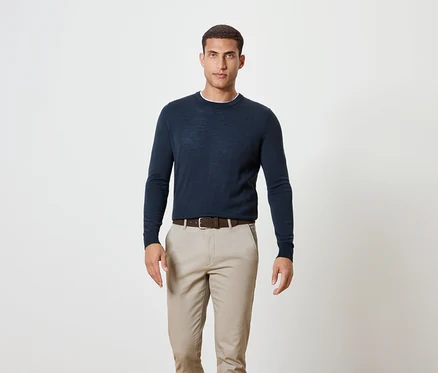Un homme debout portant un pull bleu marine, une ceinture marron et un pantalon kaki.