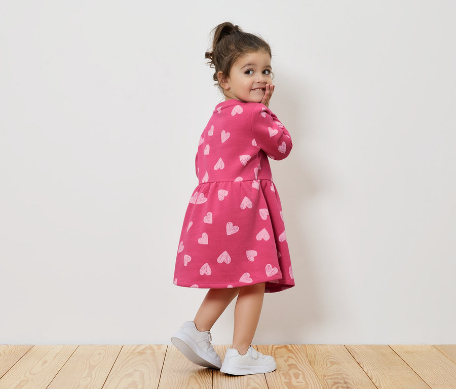 Fillette en robe rose à motifs de cœurs et baskets blanches regardant par-dessus son épaule.