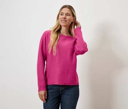 Une femme arrange ses cheveux, porte un pull rose et un jean.