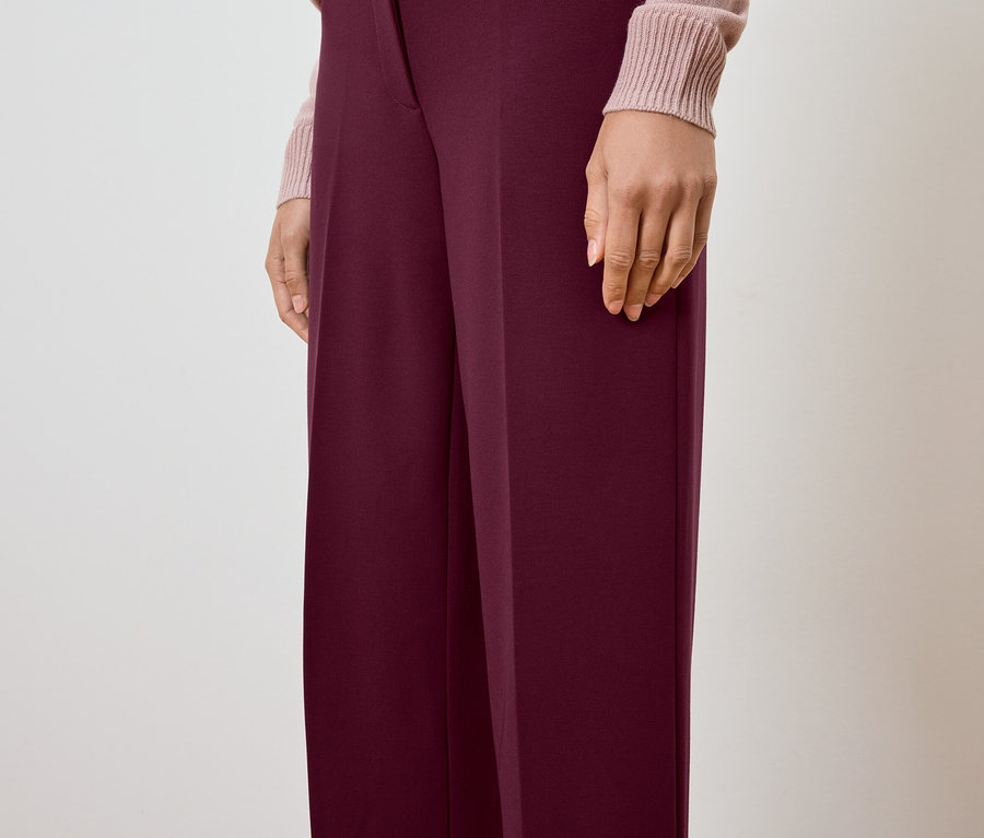 Vue partielle d'une personne portant un pantalon bordeaux et un pull rose clair.