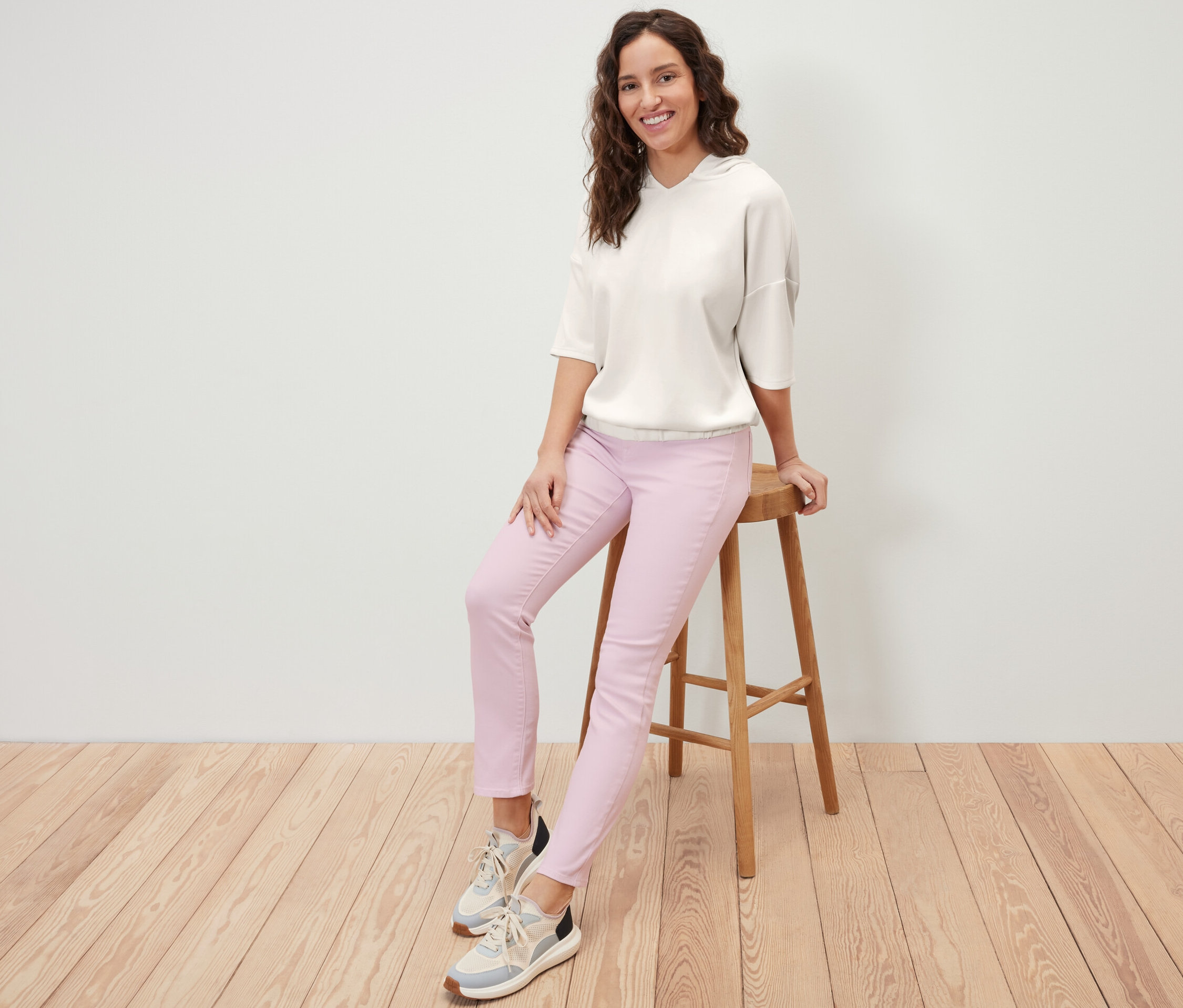 Femme assise sur un tabouret portant un pull à capuche en mélange de modal crème et un pantalon rose.