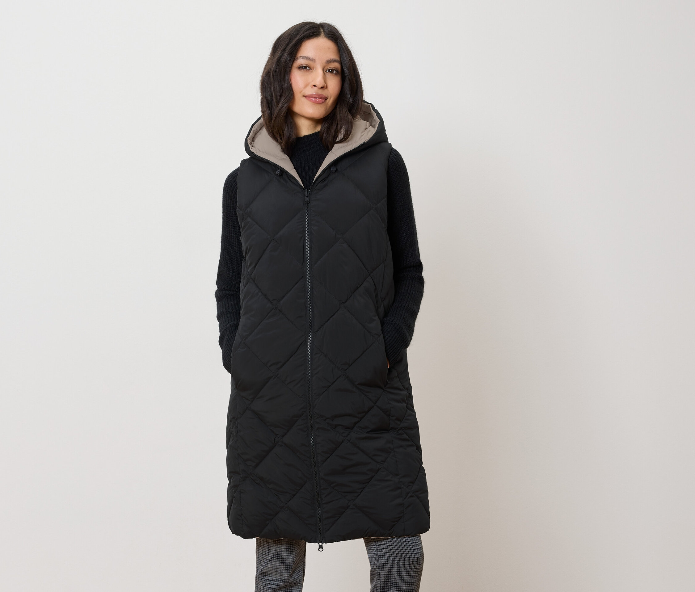 Une femme porte un long gilet noir matelassé à capuche.