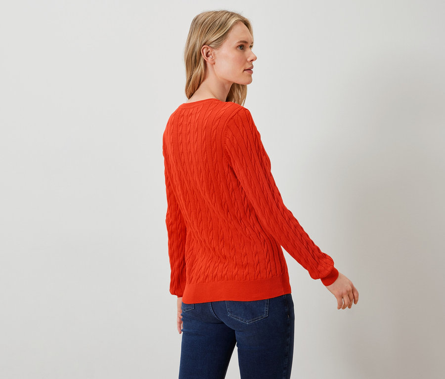 Une femme pose en pull orange et jean bleu.