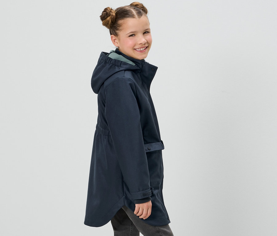 Une fillette souriante pose en manteau softshell marine pour enfants et en jean gris.