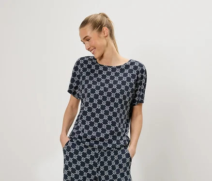 Une femme blonde porte un haut bleu à manches courtes avec un motif géométrique blanc et un pantalon assorti.