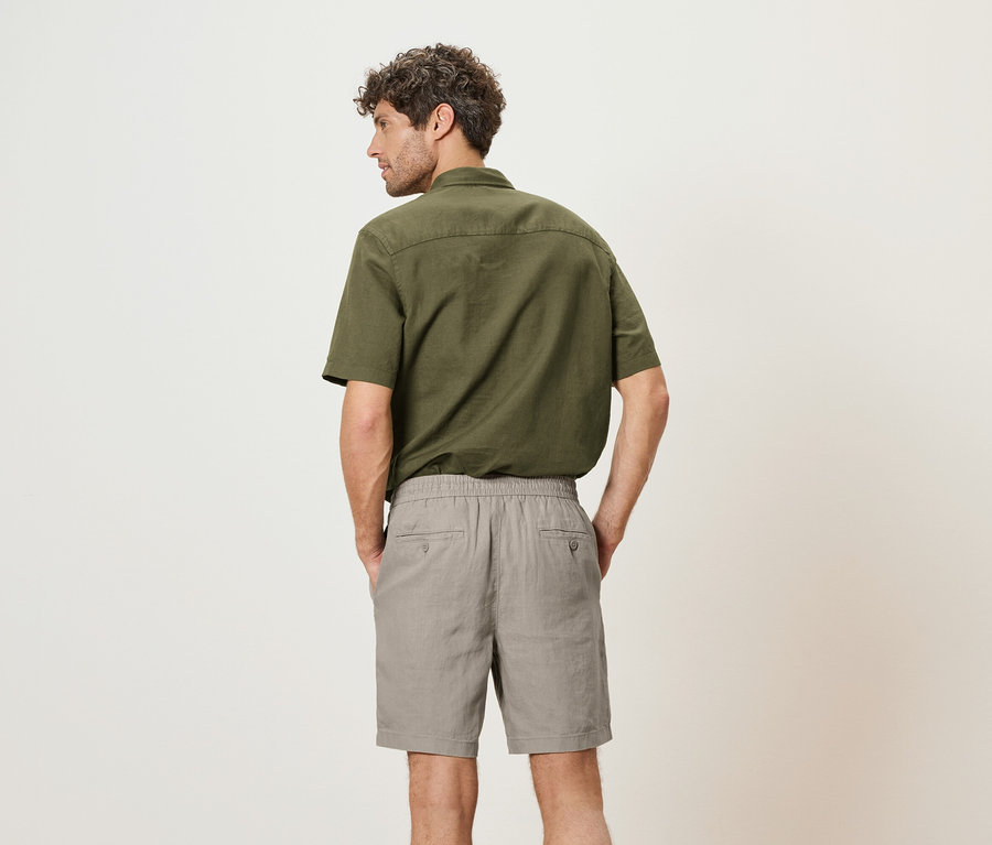 Un homme vu de dos, portant une chemise verte et un short gris.
