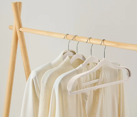 Des vêtements clairs sont suspendus à un portant en bois.
