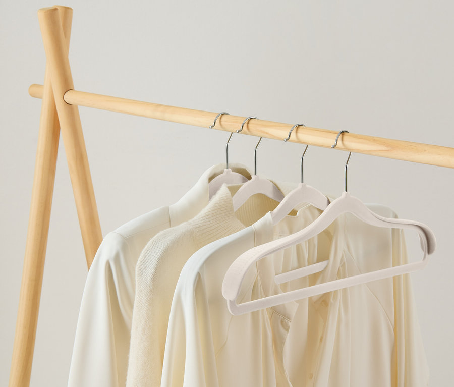 Des vêtements clairs sont suspendus à un portant en bois.