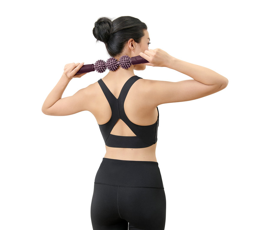 Une femme masse son cou avec un rouleau de massage violet à picots.