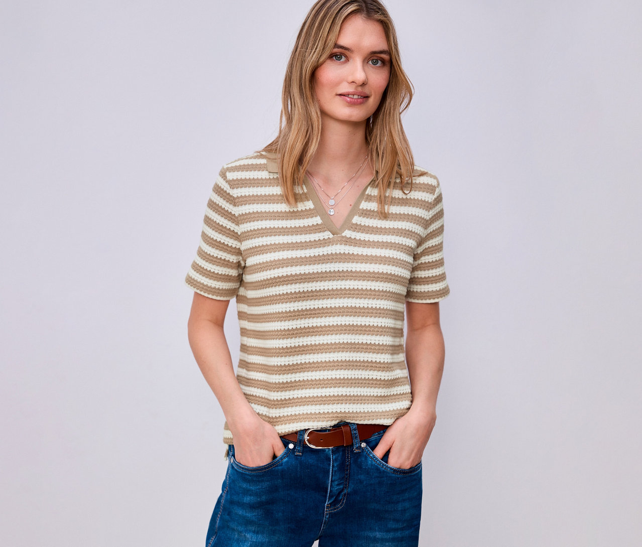 Une femme portant un jean et une ceinture marron porte un pull en maille Street One rayé avec un col en V.