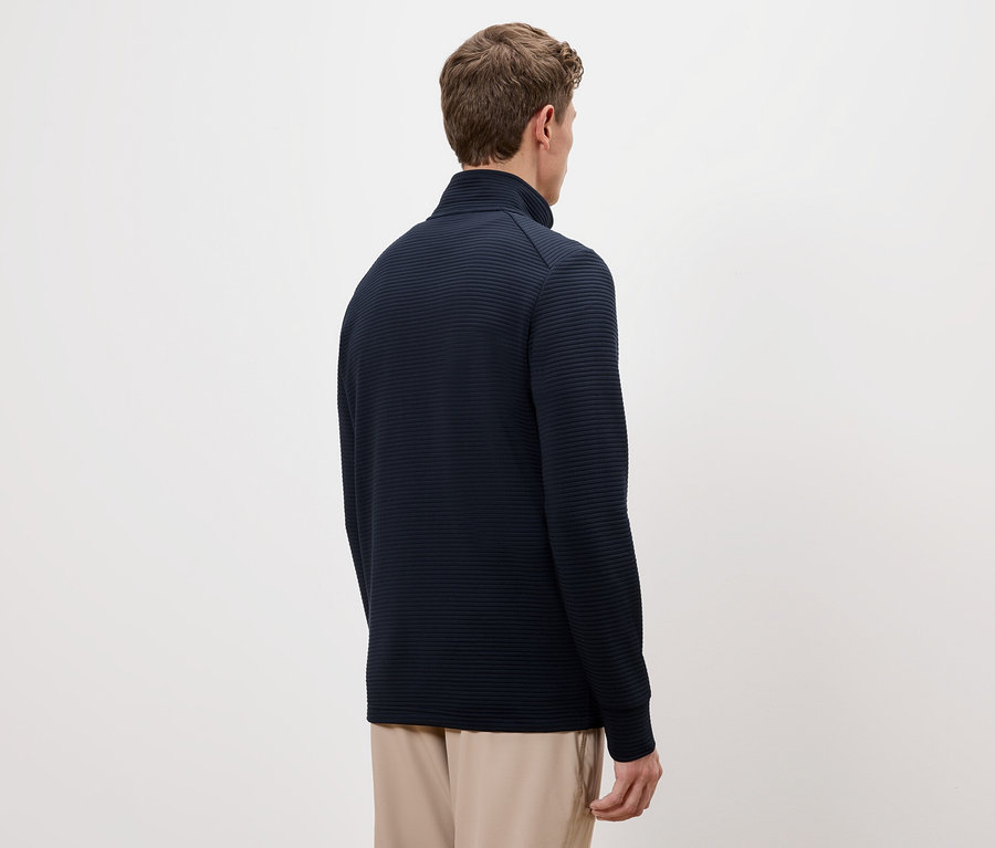 Vue arrière d'un homme aux cheveux bruns portant un pull bleu marine à col montant et un pantalon beige.