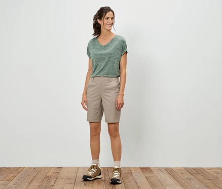 Une femme se tient debout et porte un t-shirt vert, un short et des chaussures de randonnée.