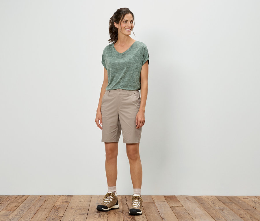 Une femme se tient debout et porte un t-shirt vert, un short et des chaussures de randonnée.