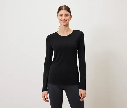 Une femme porte un t-shirt noir à manches longues et un legging foncé sur un fond blanc.