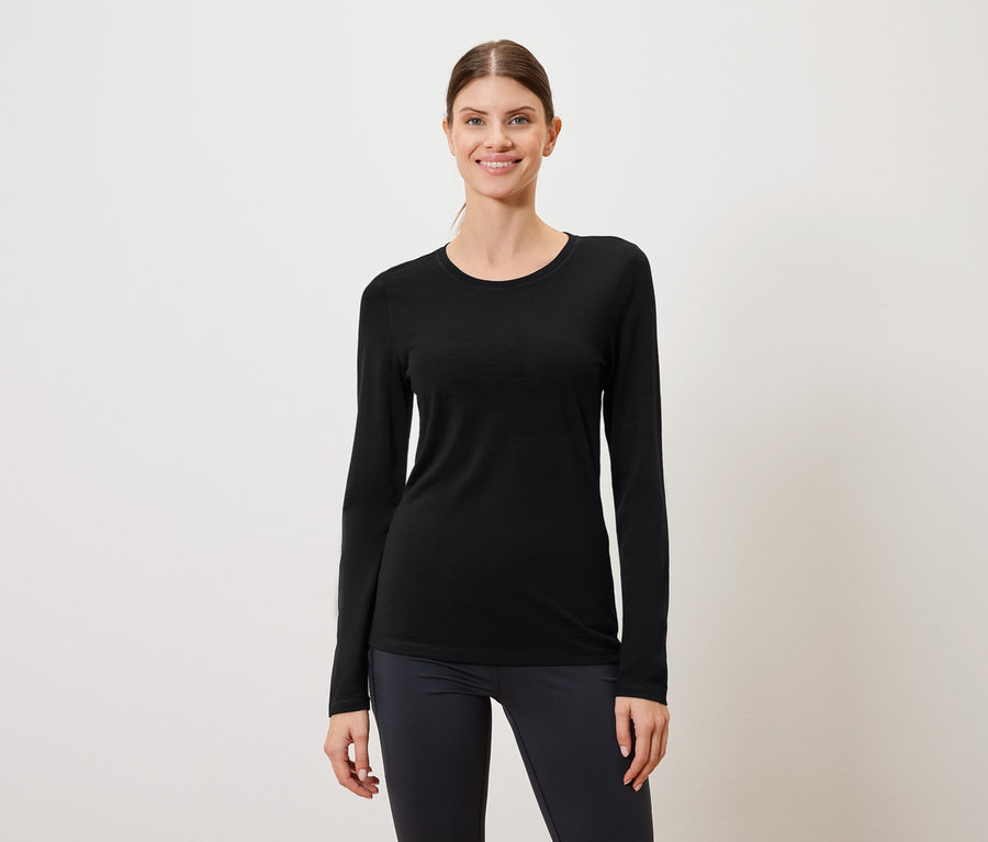 Une femme porte un t-shirt noir à manches longues et un legging foncé sur un fond blanc.