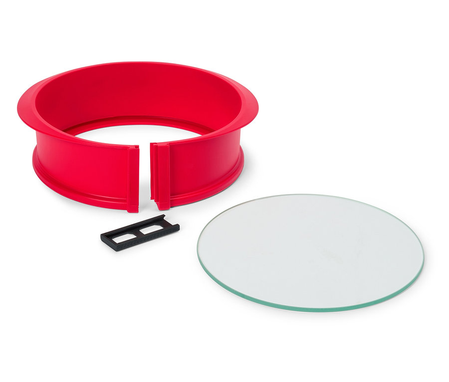 Un cercle à pâtisserie rouge avec un clip noir et une plaque de verre circulaire sur un fond blanc.