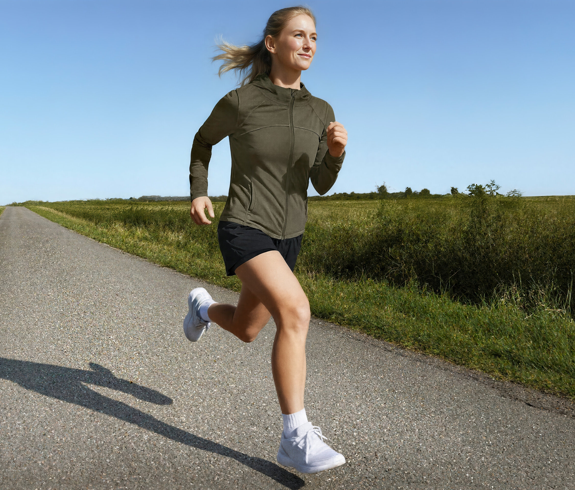 Femme courant sur une route de campagne en veste de sport et short de course 2 en 1.
