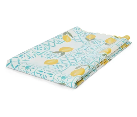 Un tissu plié avec un motif de citrons et des ornements turquoise est posé sur un fond blanc.