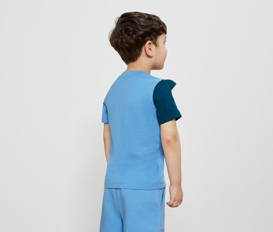 Vue arrière d'un garçon aux cheveux bruns portant un t-shirt et un short bleus, avec une manche bleu marine sur le côté gauche.