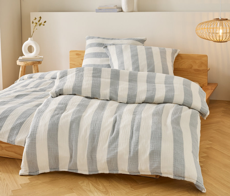 Lit avec des draps et des oreillers à rayures bleues et blanches sur un cadre de lit en bois. Une lampe est suspendue au-dessus du lit.
