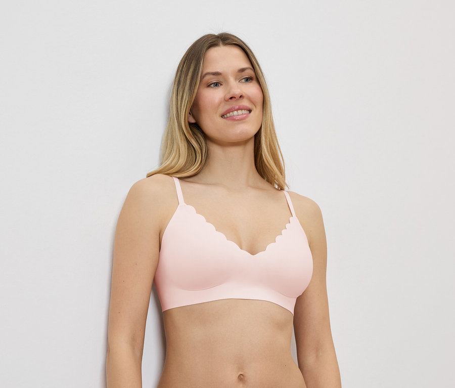 Une femme blonde porte un soutien-gorge rose clair à décolleté ondulé et regarde sur le côté.