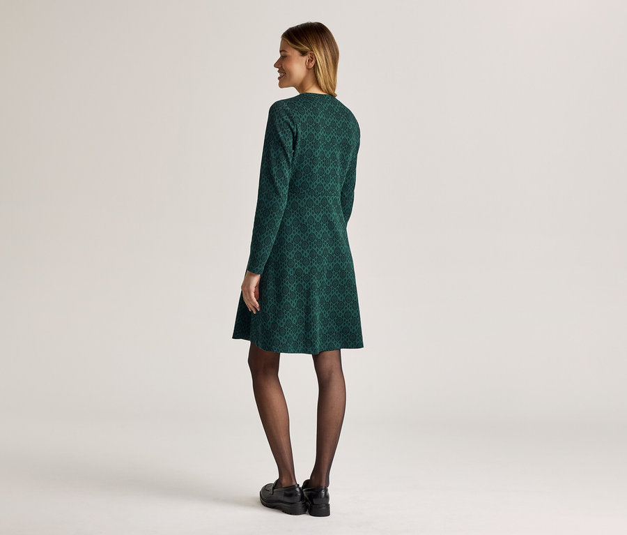 Femme vue de dos portant une robe verte à motifs à manches longues, des collants noirs et des chaussures.