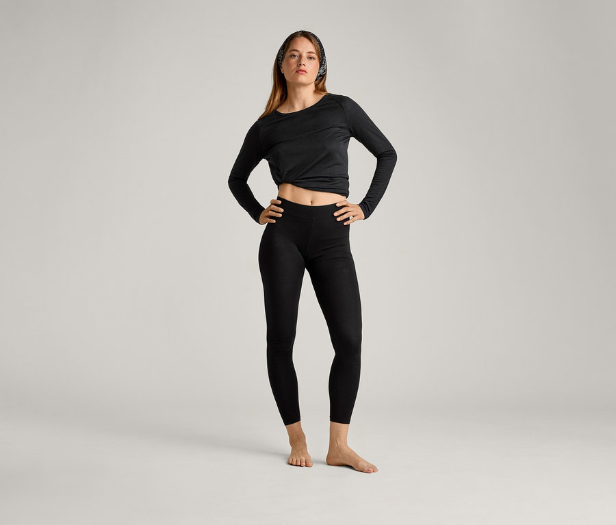 Une femme portant un haut noir et des leggings de sport pose, les mains sur les hanches.