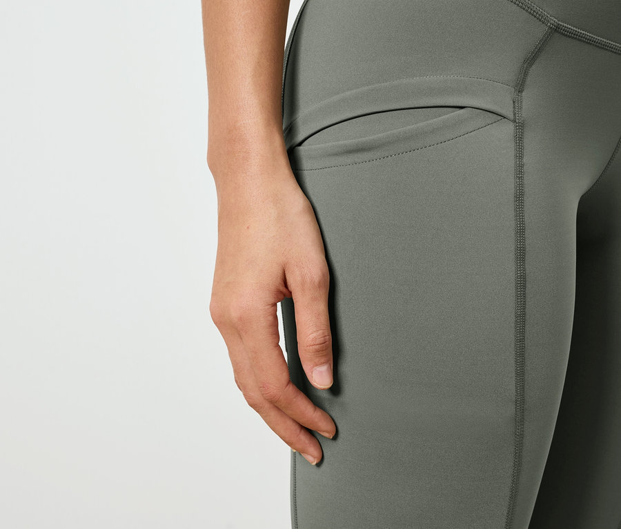 Gros plan d'une personne portant un legging vert olive avec une poche latérale.