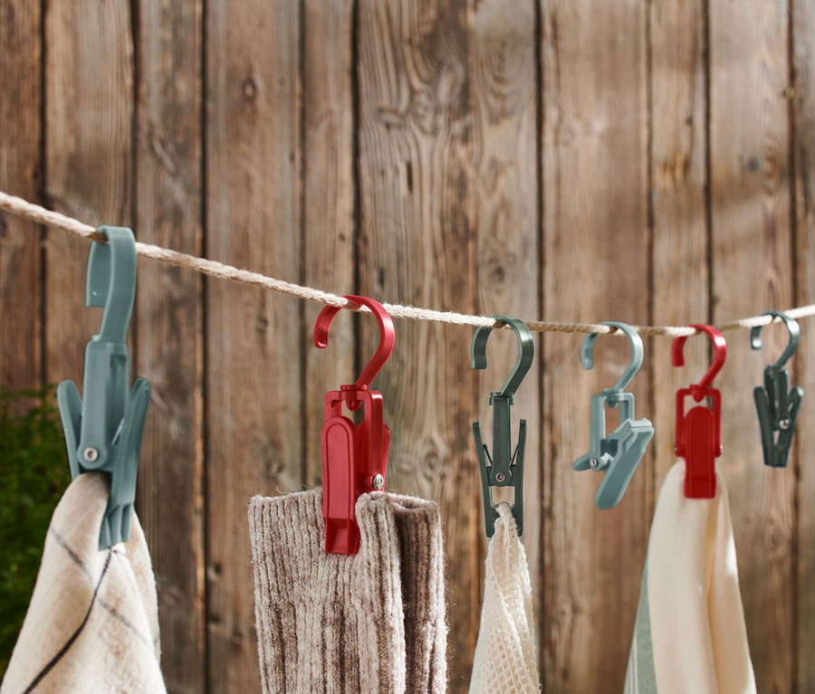 Des pinces à linge multicolores sont suspendues à une corde à linge devant un mur en bois.