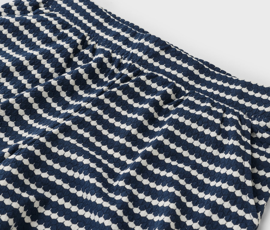 Gros plan sur une partie d'un pantalon bleu marine avec des motifs géométriques blancs.