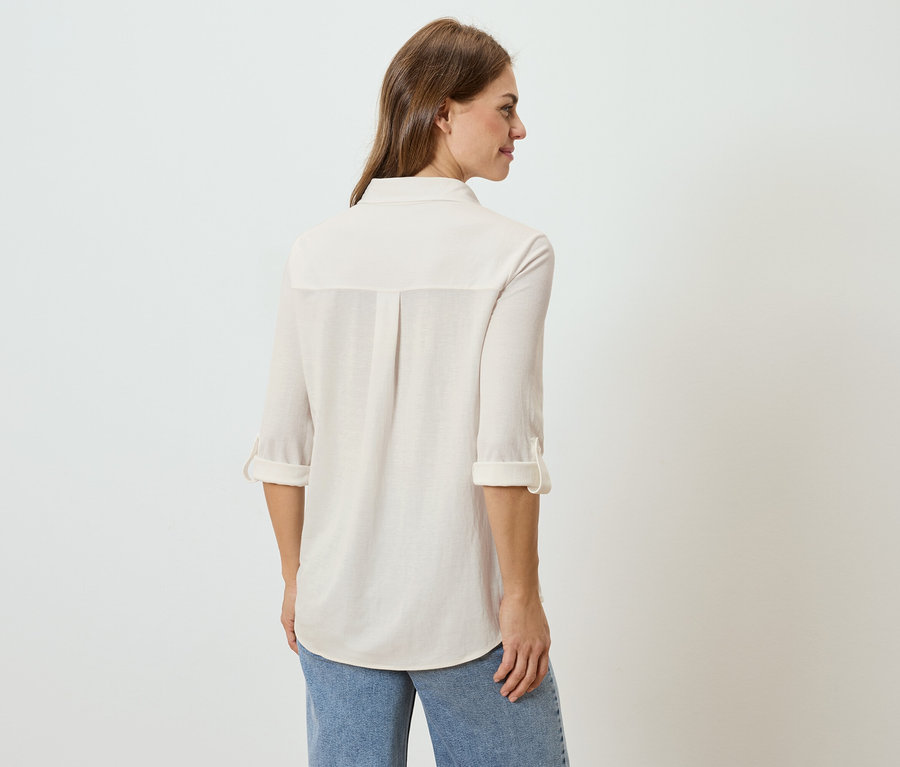 Vue arrière d'une femme aux longs cheveux bruns portant une chemise claire et un jean.