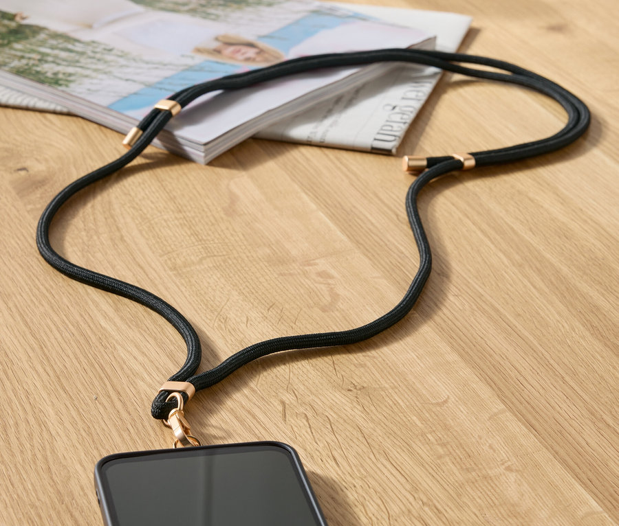 Une chaîne de téléphone noire avec des détails dorés est posée sur une table à côté d'un magazine et d'un sac à main beige.