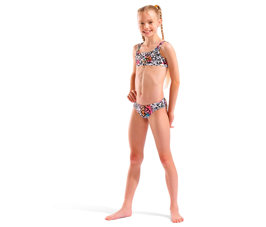 Fillette blonde avec des tresses, portant un bikini blanc à motifs colorés, souriant.