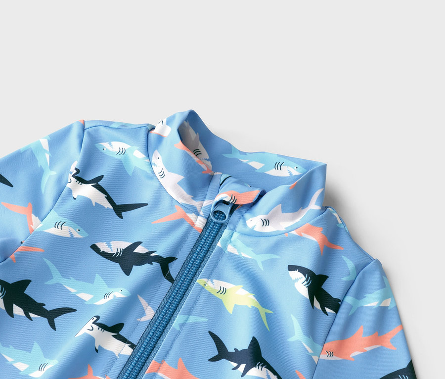 Gros plan d'un maillot de bain bleu clair à manches longues, avec un motif de requins sur toute la surface et une fermeture éclair bleue.