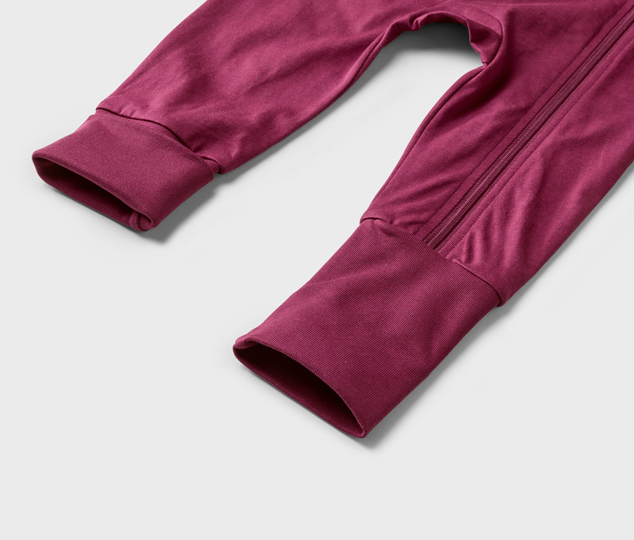 Gros plan sur les manches et les jambes d'une combinaison bordeaux zippée.