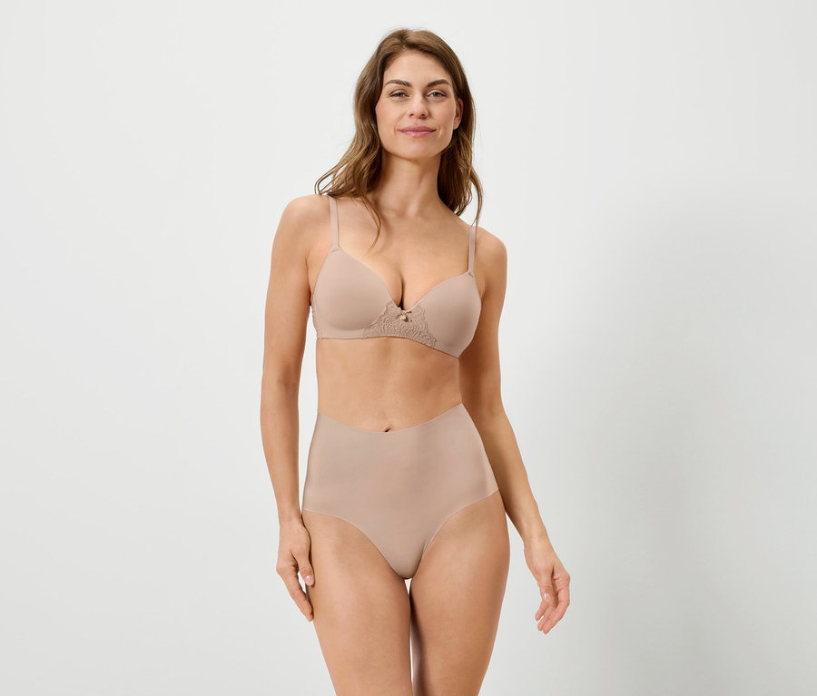 Une femme porte un soutien-gorge et une culotte couleur chair sur fond blanc.