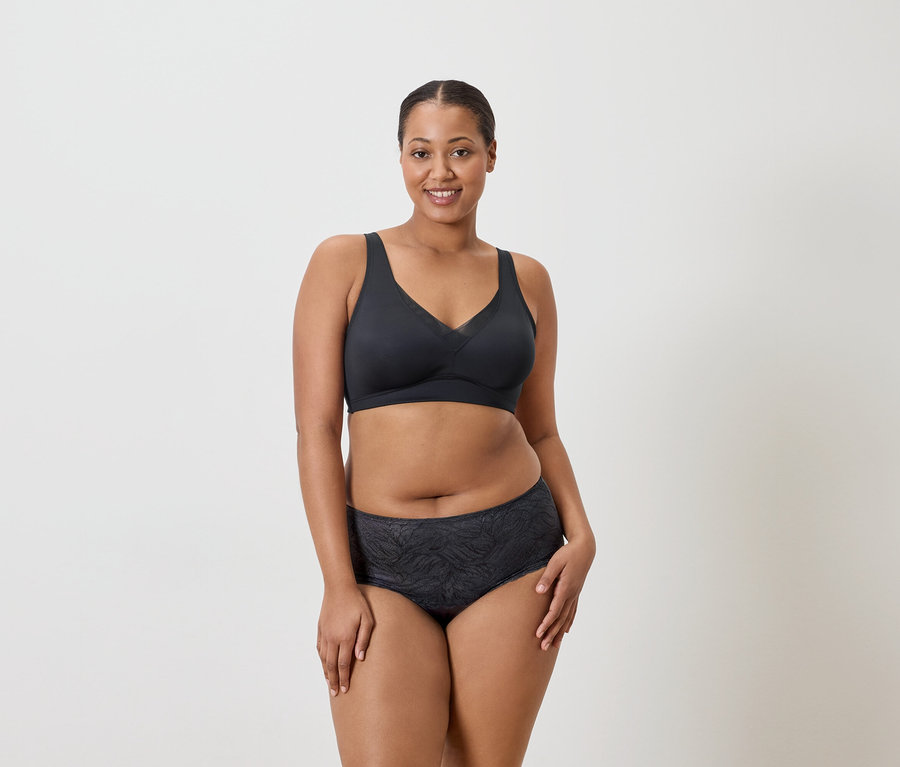 Femme portant un soutien-gorge de sport foncé et une culotte à motifs sur un fond neutre.