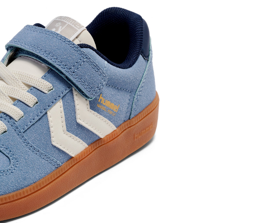 Gros plan d'une seule basket Hummel bleu clair avec fermeture Velcro et chevrons blancs sur une semelle marron.