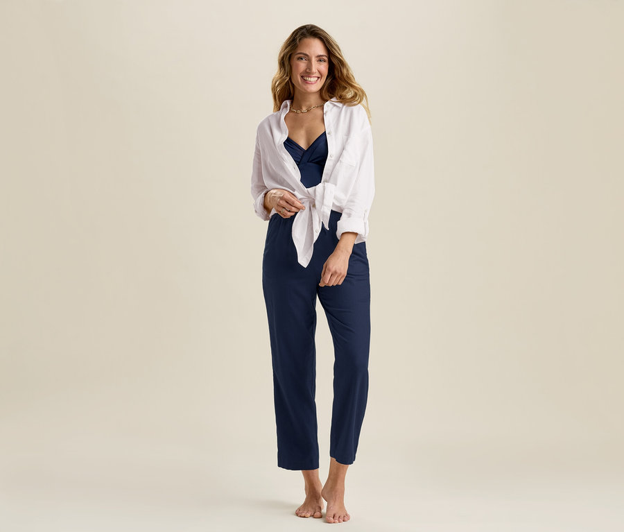 Une femme porte une blouse longue en lin blanche et un pantalon en lin bleu marine.