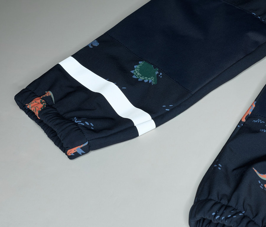 Gros plan sur des jambes de pantalon bleu marine à motif de dinosaures avec une bande blanche sur fond gris.