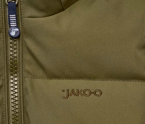 Gros plan d'une veste ou d'un gilet vert olive, montrant une fermeture éclair avec une tirette bleu foncé ornée d'un petit charm d'oiseau et le logo "JAKO-O" brodé en marron.