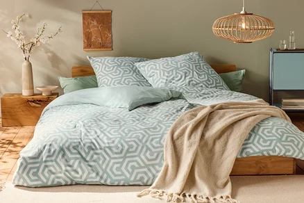 Lit avec parure de lit en jersey de taille normale, avec motif géométrique et coussins vert clair.