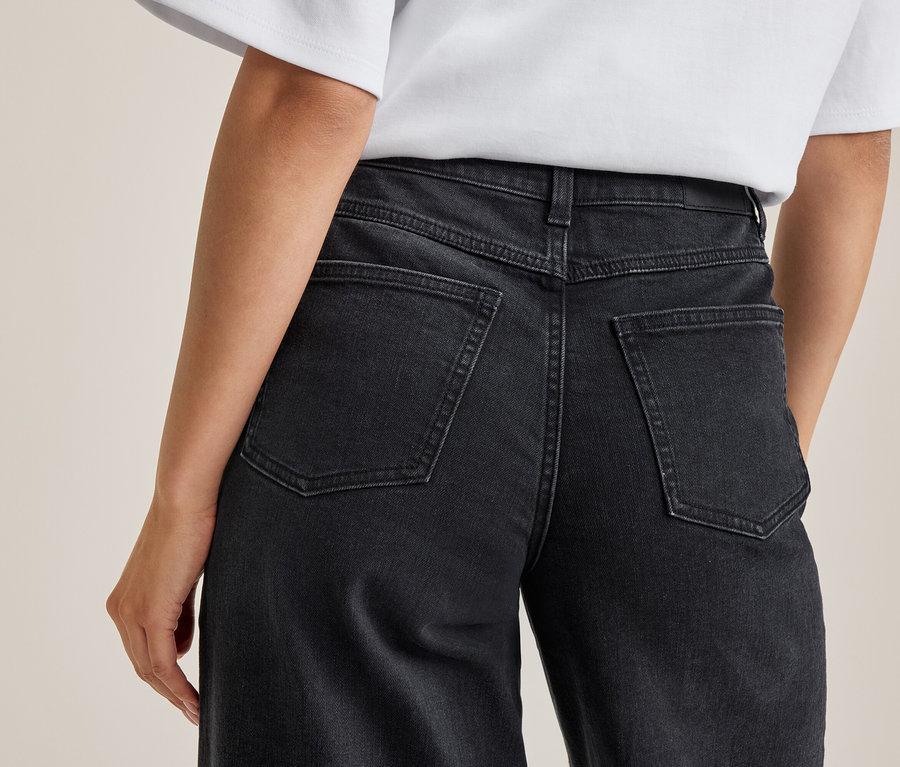 Vue de dos d'une personne portant un jean gris foncé et un t-shirt blanc. Le jean a des poches arrière et des coutures visibles.