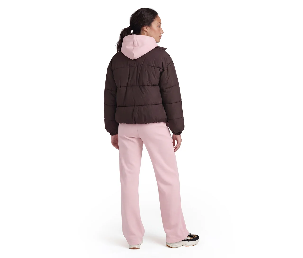 Personne de dos portant une doudoune marron sur un sweat à capuche rose, un pantalon de jogging rose et des baskets.